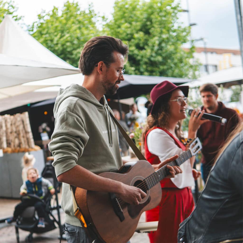 Man speelt gitaar tijdens markt met muzikale sfeer.