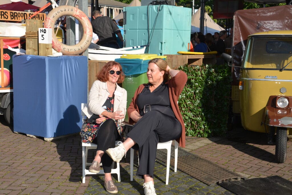 Twee vrouwen genieten van het festival Heerlijk Heesch op een zonnige dag.
