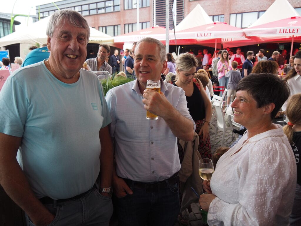 Gezellige markt in Heesch met mensen die genieten van eten en drinken onder parasols.