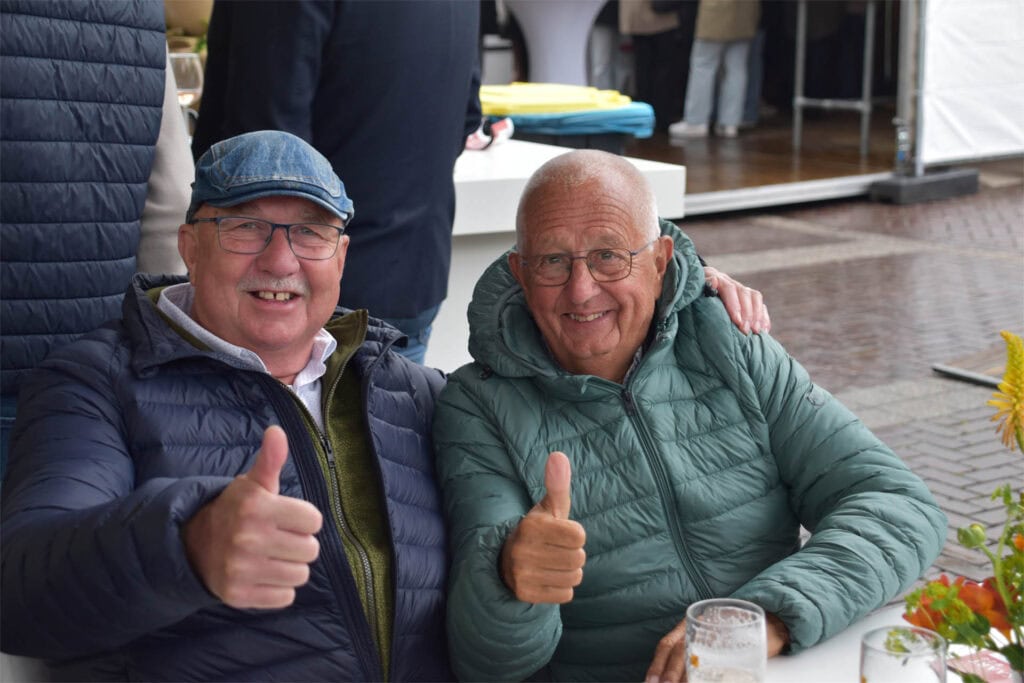 Twee lachende mannen met duimen omhoog tijdens Heerlijk Heesch evenement.