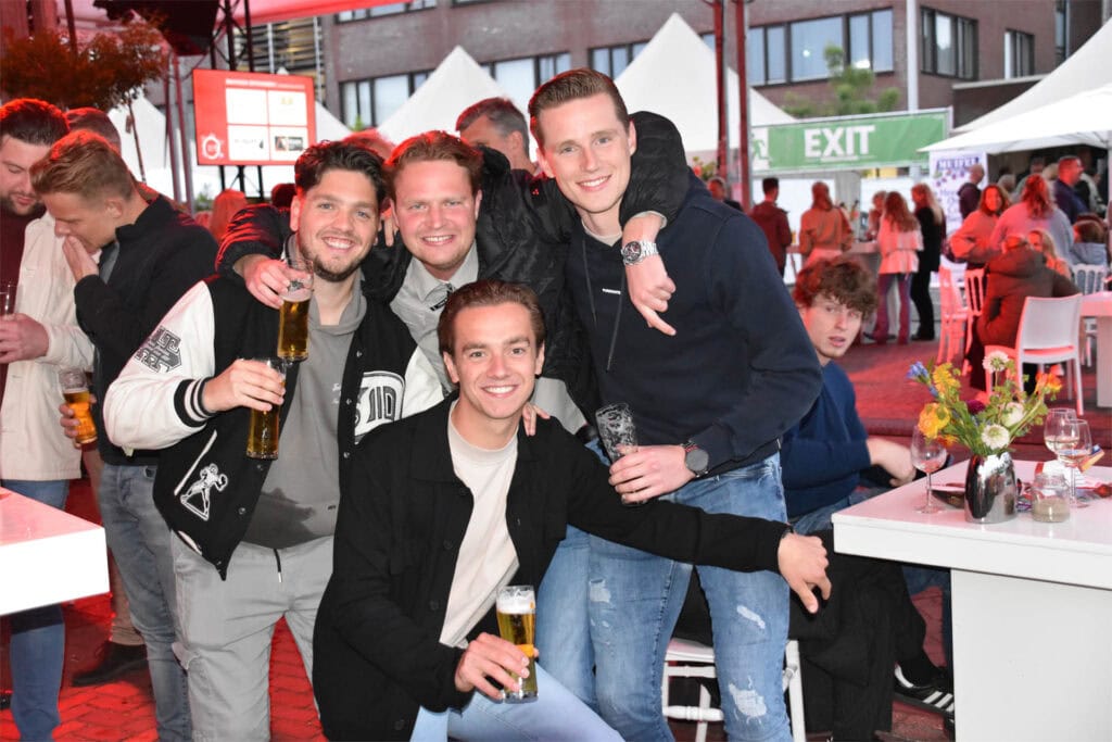 Gezellige vrienden met drankjes bij Heerlijk Heesch festival in een bruisende sfeer.