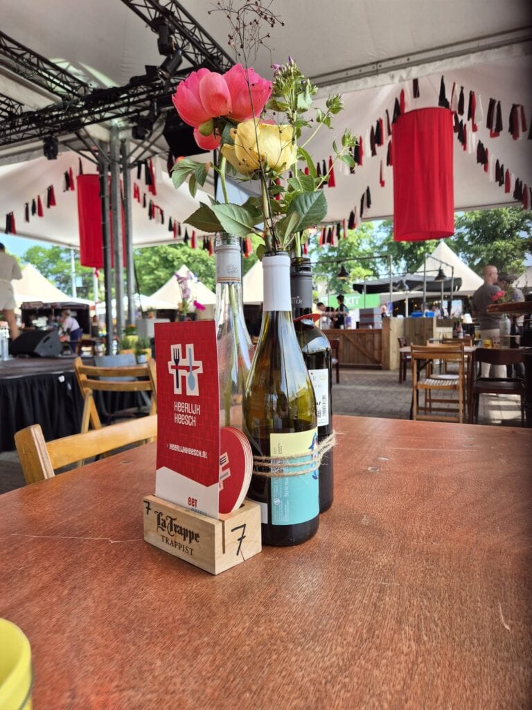Bloemen in wijnfles op tafel tijdens Heerlijk Heesch festival.