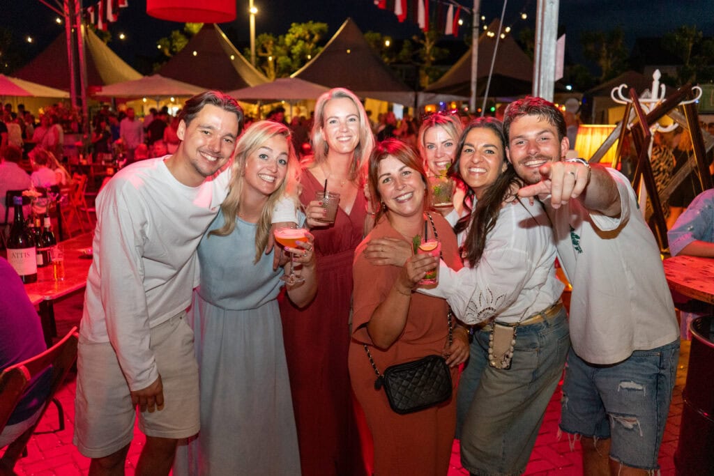 Gezellige groep vrienden genieten van feestavond in Heerlijk Heesch met drankjes en muziek.